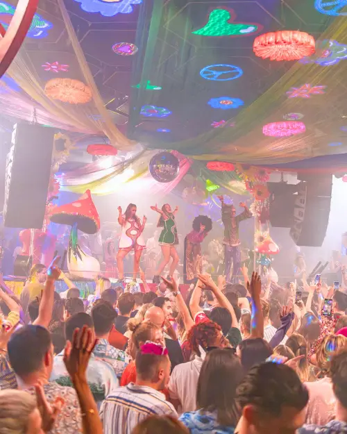 Free spirited people dancing on a stage with a crowd watching below at Flower Power club night at Pacha, which is one of the parties with the best disco in Ibiza