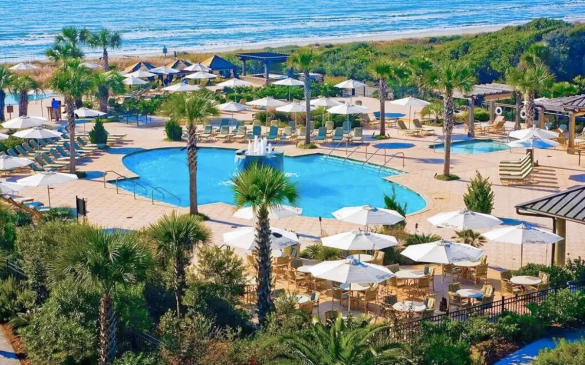 An aerial shot of Kiawah Island Golf Resort's main pool right along the beach under a sunny sky, to show how beautiful of a resort it is