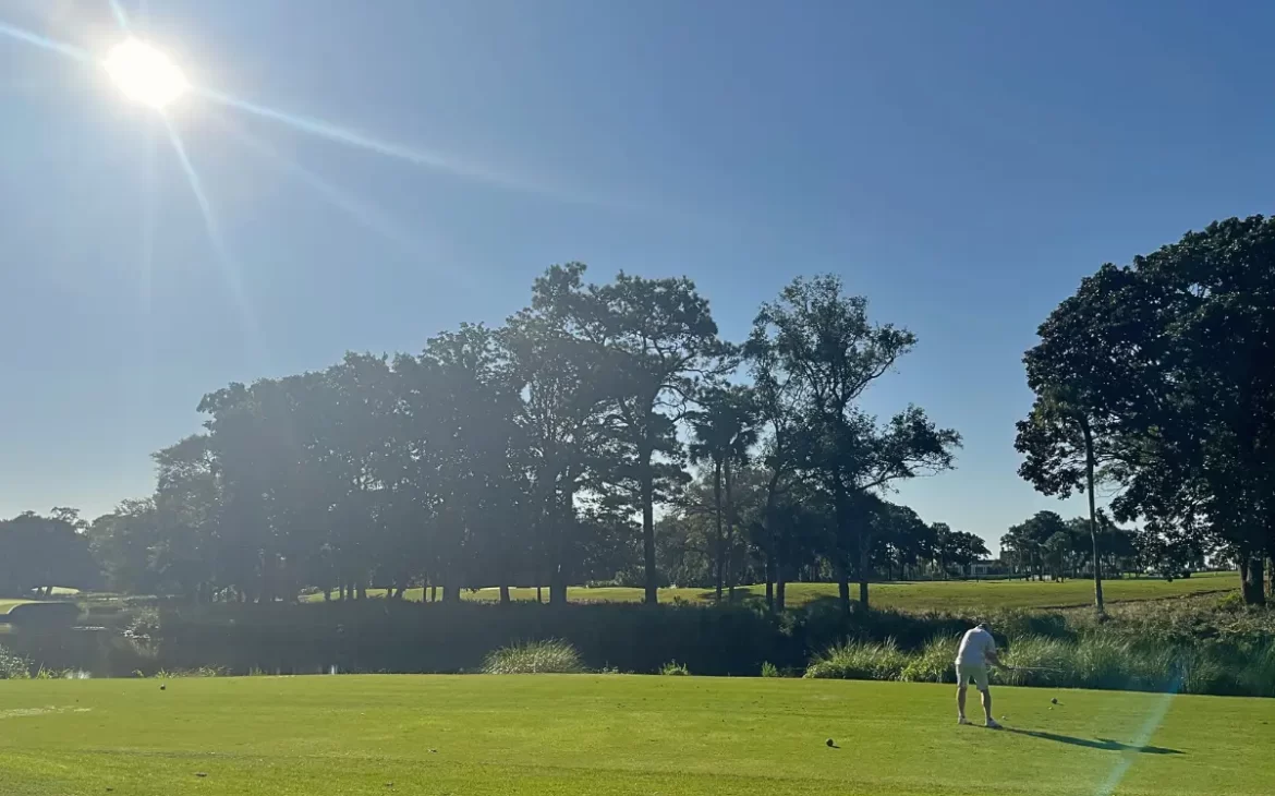 Scenic photograph of a man about to take his shot on Cougar Point golf with the bright sun shining down and bright green grass to show how beautiful the course is